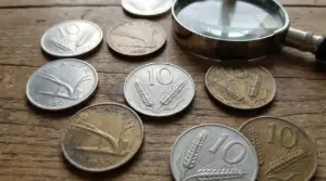Monete italiane da 10 lire con la spiga su un tavolo di legno accanto a una lente d’ingrandimento