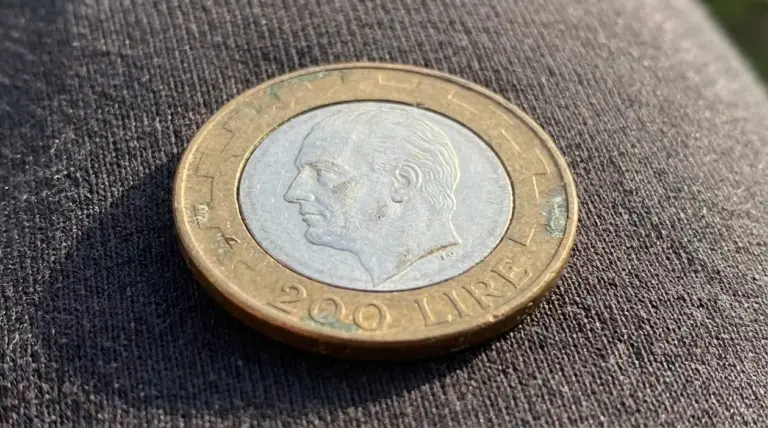 Moneta da 200 lire italiane appoggiata su un tessuto scuro, fotografata in primo piano