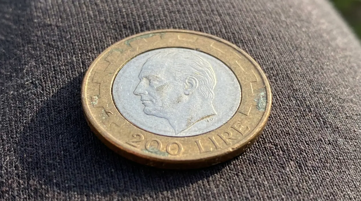 Moneta da 200 lire italiane appoggiata su un tessuto scuro, fotografata in primo piano