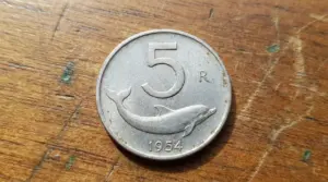 Moneta da 5 lire del 1954 con delfino, appoggiata su una superficie di legno