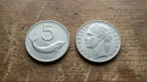 Moneta italiana da 5 lire del 1956 con delfino, mostrata fronte e retro su un tavolo di legno