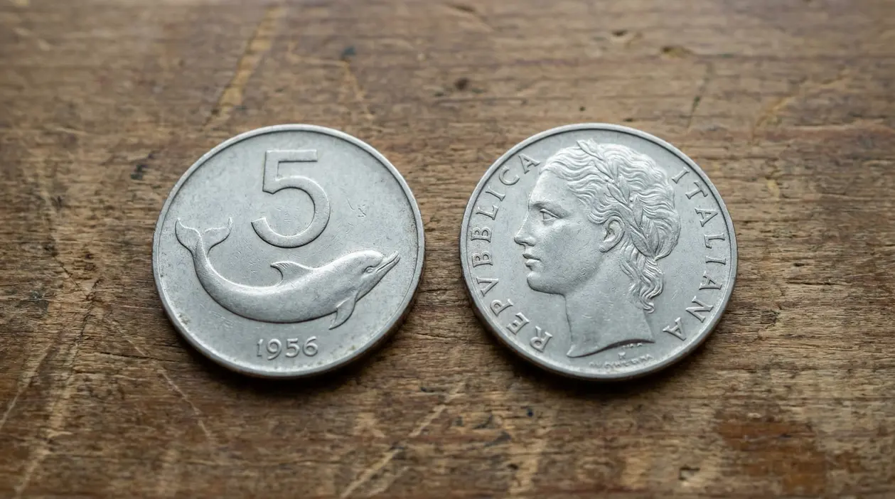 Moneta italiana da 5 lire del 1956 con delfino, mostrata fronte e retro su un tavolo di legno