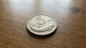 Moneta da 5 lire con delfino del 1956 appoggiata su un tavolo di legno