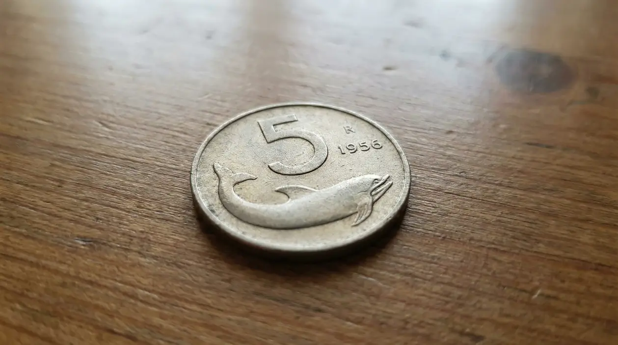 Moneta da 5 lire con delfino del 1956 appoggiata su un tavolo di legno