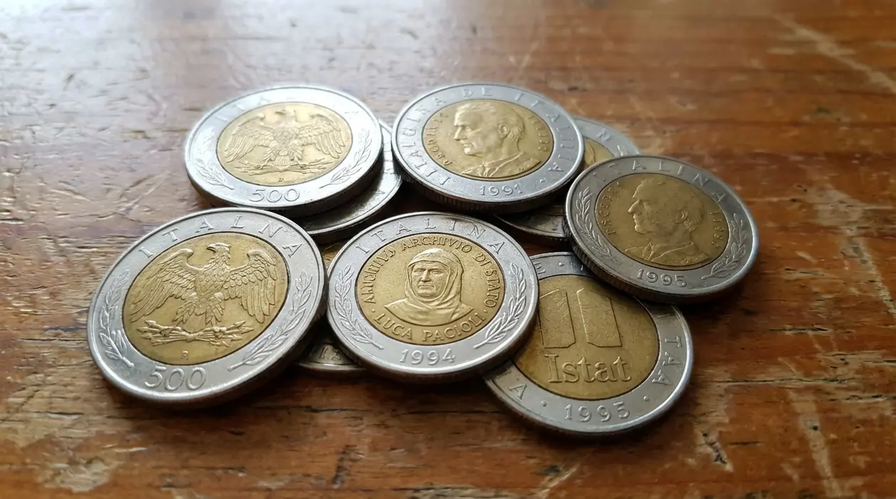Alcune monete italiane da 500 lire bimetalliche appoggiate su un tavolo di legno