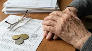 Mani di una persona anziana su documenti contabili con occhiali e monete, tema aumento pensioni