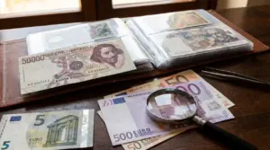 Album con banconote da collezione italiane ed euro su un tavolo, con lente d’ingrandimento per valutarne il valore