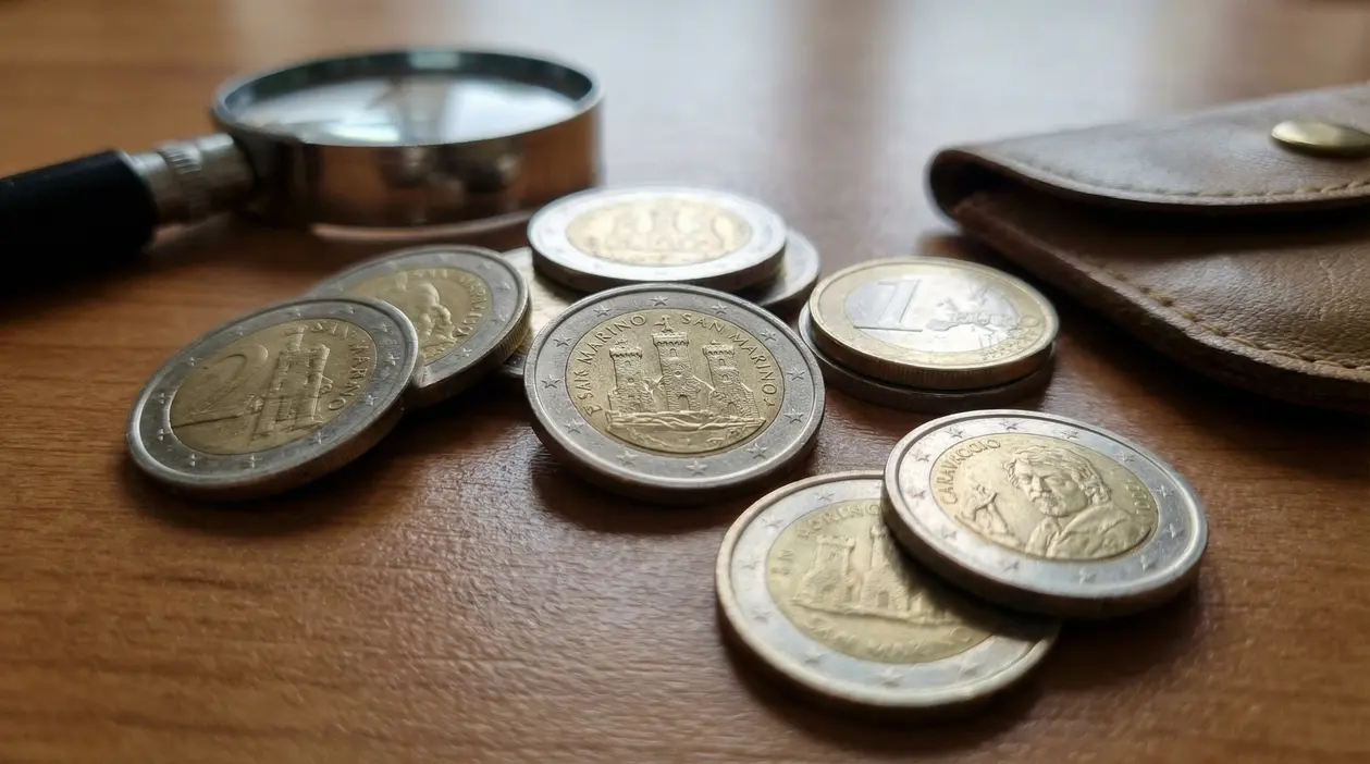Monete da 2 euro di San Marino su un tavolo accanto a una lente d’ingrandimento e a un portamonete