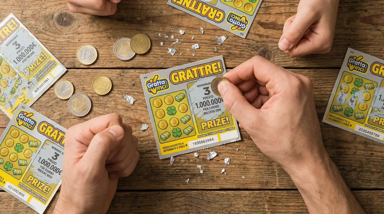 Mani che grattano un biglietto Gratta e Vinci su un tavolo di legno con monete e coriandoli argentati
