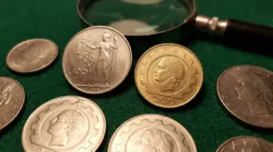 Monete in lire italiane con lente d’ingrandimento su panno verde, tra cui 100 e 200 lire da collezione
