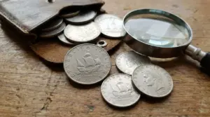 Vecchie monete da 500 lire d’argento su un tavolo, accanto a un portamonete e una lente d’ingrandimento