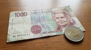 Banconota da 1000 lire Montessori usurata su un tavolo, accanto a una moneta da 2 euro