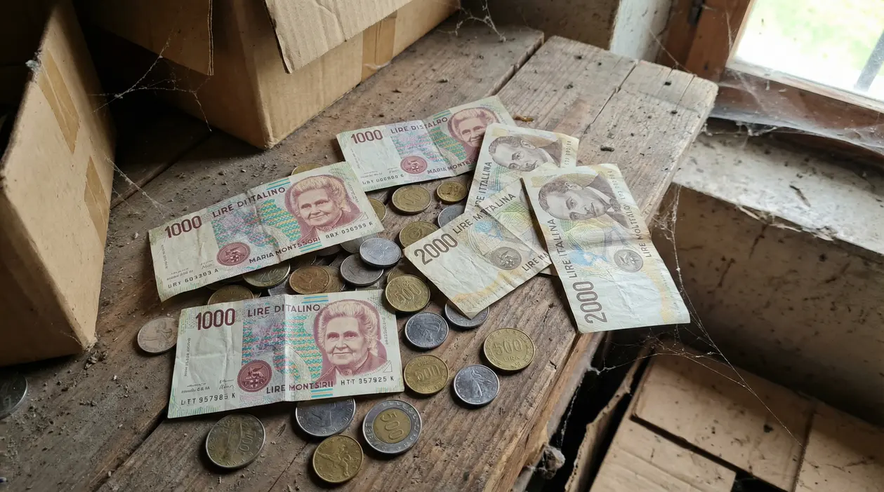 Vecchie lire italiane in banconote e monete trovate su un tavolo impolverato in soffitta
